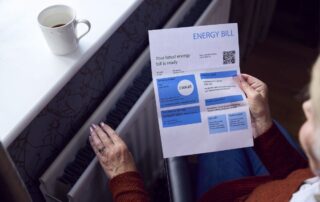 Osoba trzyma rachunek za energię i dotyka kaloryfera, myśląc o wysokich rachunkach za c.o.