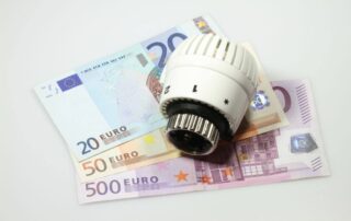 Termostat leży na banknotach euro, symbolizując dopłatę za ogrzewanie.