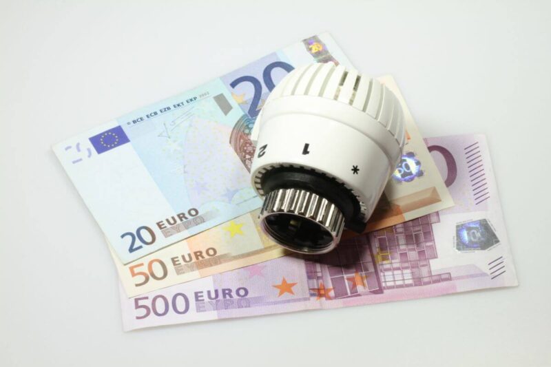 Termostat leży na banknotach euro, symbolizując dopłatę za ogrzewanie.